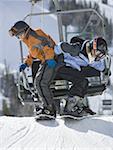 Profile of a boy and his sister snowboarding near a ski lift