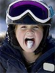 Young girl in winter with snow on tongue and ski goggles
