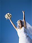 Portrait d'une jeune mariée, tenant un bouquet de fleurs avec ses bras levés