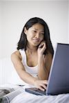 Close-up of a mid adult woman using a laptop computer while talking on a mobile phone