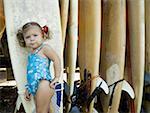 Portrait of a baby girl leaning against a surfboard