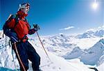 Downhill skier with goggles standing on mountain with ski poles smiling
