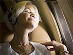 Close-up of senior woman wearing headphones and sleeping in an airplane