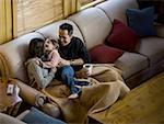 Woman and man snuggling with young girl on sofa