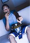Teenage boy watching television and eating popcorn
