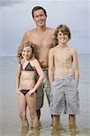 Porträt von einem Vater und seinen beiden Kindern im Wasser stehend