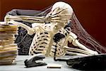 Skeleton sitting at desk talking on telephone with webs and stacks of paperwork