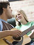 Close-up of a teenage boy playing a guitar with a teenage girl