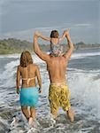 Rear view of a man and a  woman walking on the beach with their daughter