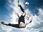 Soccer player kicks ball while silhouetted against a cloudy blue sky