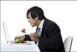 Voir le profil:: un homme d'affaires manger tout en utilisant un ordinateur portable