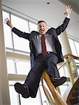 Happy businessman sliding down stair railing