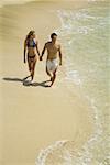 Vue grand angle sur un jeune couple, main dans la main et en marchant sur la plage