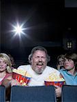 Large man with buckets of popcorn and drink at movie theater between couple