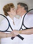 Close-up of a senior couple holding tennis rackets and kissing