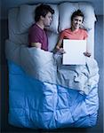 Mann schlafend im Bett und Frau hält lächelnd leer Zeichen