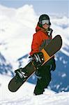 Snowboarder standing on mountain with snowboard