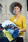 Femme avec des vêtements dans le panier à linge à la laverie souriant