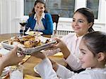 Two sisters passing a tray of food at a dinning table