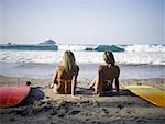 Rear view of two young women sitting together on the beach