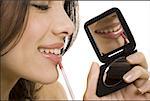 Closeup of woman applying lipstick with compact mirror