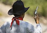 Rear view of a boy in a cowboy costume holding a toy gun