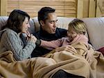 Man and woman snuggling with young girl on sofa with blanket