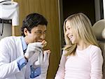 Male dentist holding false teeth talking to girl