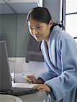 Profile of a mid adult woman looking at a laptop in the bathroom