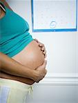 Profile of a pregnant woman touching her stomach in front of a calendar