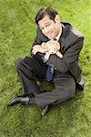 High angle view of a businessman with hugging a toy sitting on a grass