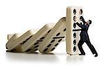 Businessman holding up falling dominoes