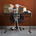 Skeleton sitting at desk with stacks of paperwork