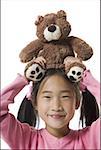 Portrait of a girl holding a teddy bear over her head and smiling
