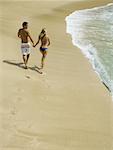 Rear view of a young couple holding hands and running on the beach