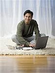 Portrait of a man sitting of the floor and using a laptop