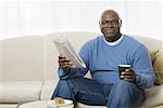 Portrait of a senior man sitting on a couch and holding a tea cup and a newspaper