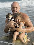 Portrait of a man holding his daughter and a puppy in the ocean