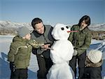 High angle view of a mid adult couple and their two children standing beside a snowman