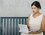 Businesswoman sitting on a bench and using a laptop