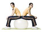 Profile of two twin teenage girls sitting on a fitness ball