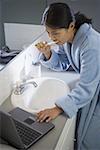High angle view of a mid adult woman brushing her teeth while using a laptop in the bathroom