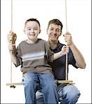 Portrait d'un garçon assis sur une balançoire avec son père derrière lui