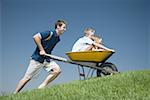 Father pushing son and daughter in a wheelbarrow