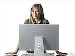 Girl with braces standing behind computer monitor