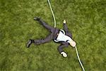 High angle view of a businessman with a hose lying down on a lawn