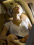 A senior woman wearing headphones and sleeping in an airplane