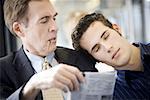 Close-up of a young man asleep on a mature man's shoulder