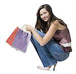 Portrait of a young woman crouching and holding shopping bags