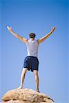 Low angle view of a young man standing on a rock with his arm outstretched